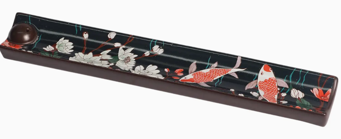 Decorative incense holder with floral and fish design on a black background